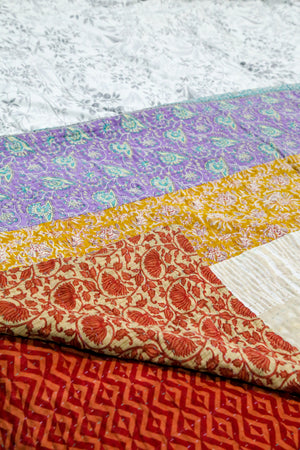A beautiful Hope Quilt made from recycled sarees, featuring intricate Kantha stitching. This vibrant quilt, designed to fit a full/queen bed, showcases a patchwork of colorful fabric pieces, each carefully hand-stitched together. The delicate Kantha stitching adds texture and depth, creating a warm, sustainable, and artistic piece for your bed.