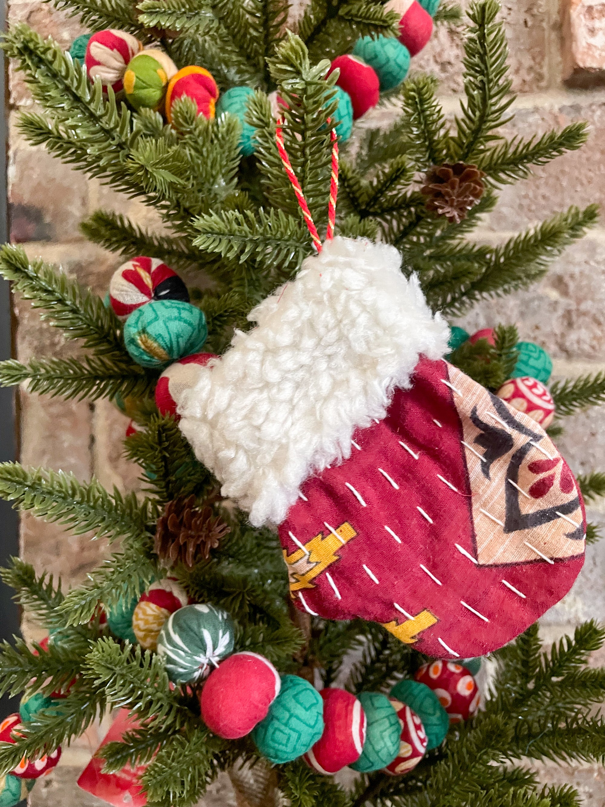 Kantha/ woll Ornament 
Alt Text 
Hand-stitched Kantha stocking, mitten, and Santa hat ornament with a wool cuff. Available in bold colors, ideal for hanging on Christmas trees.