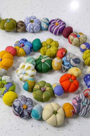 A variety of colorful handmade pumpkin-shaped garlands made from recycled saree material, displayed on a white background.