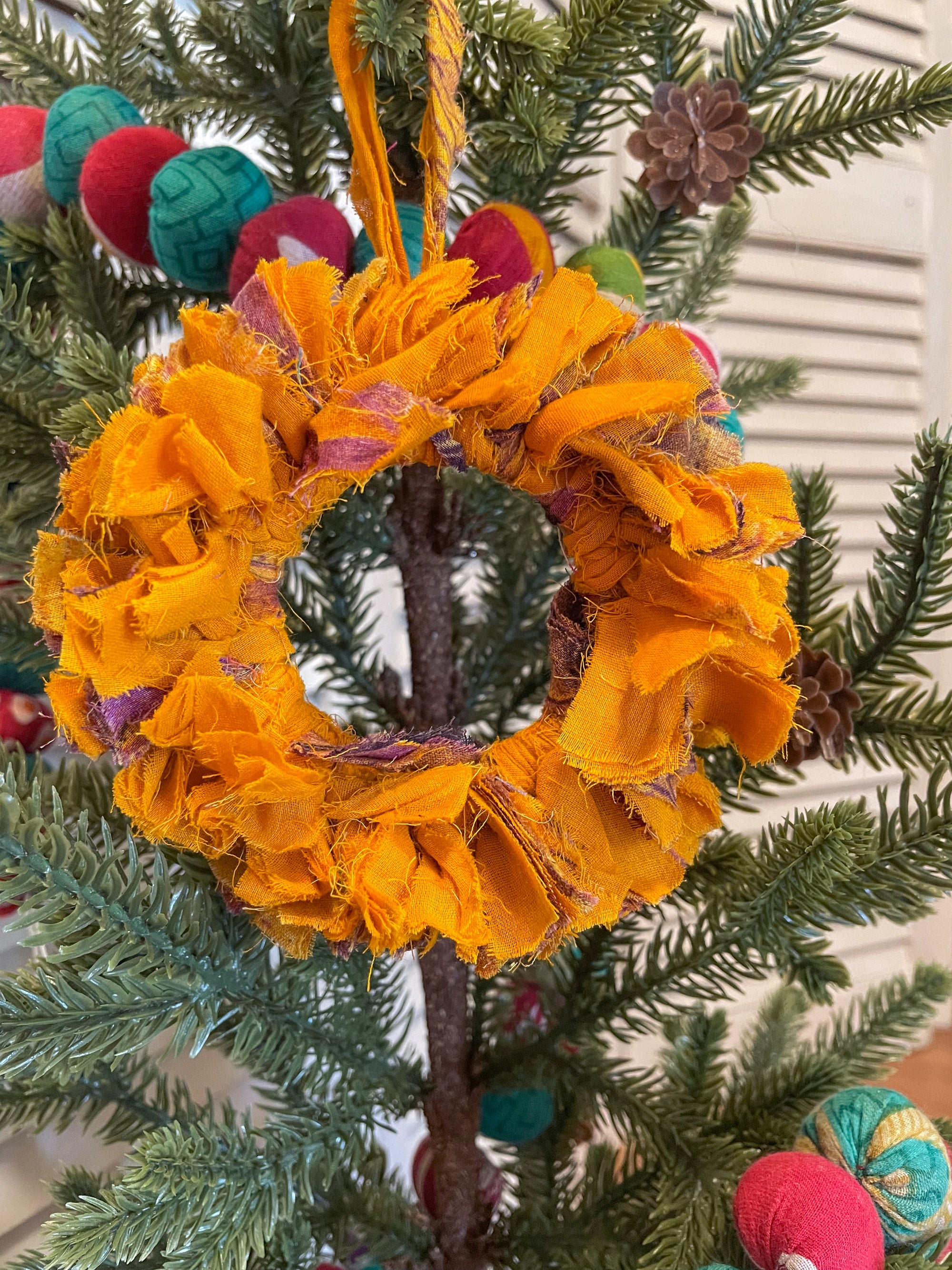 Small saree wreath ornament made from colorful hand tied saree fabric scraps, perfect for adding a vibrant and eco-friendly touch to holiday or home decor.