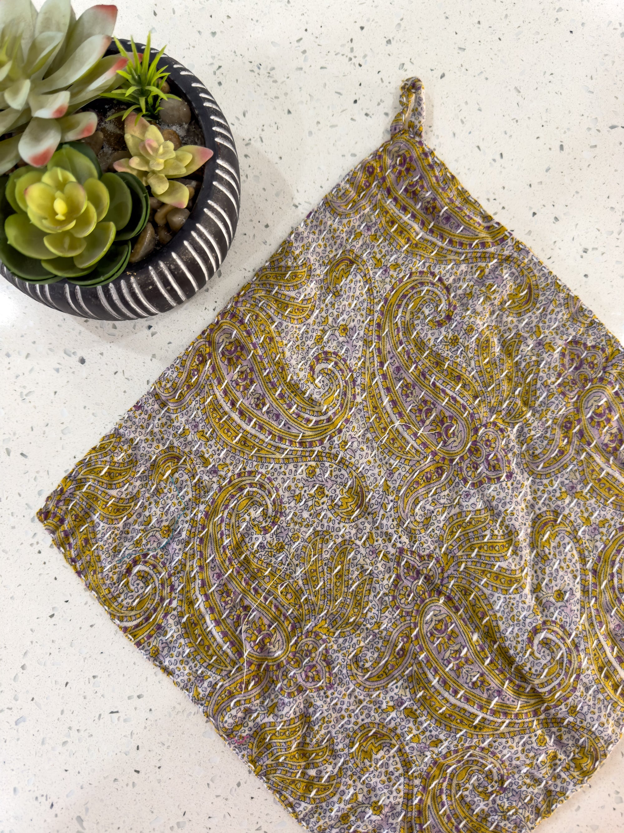 a table with a potted plant and a yellow and grey paisley print napkin