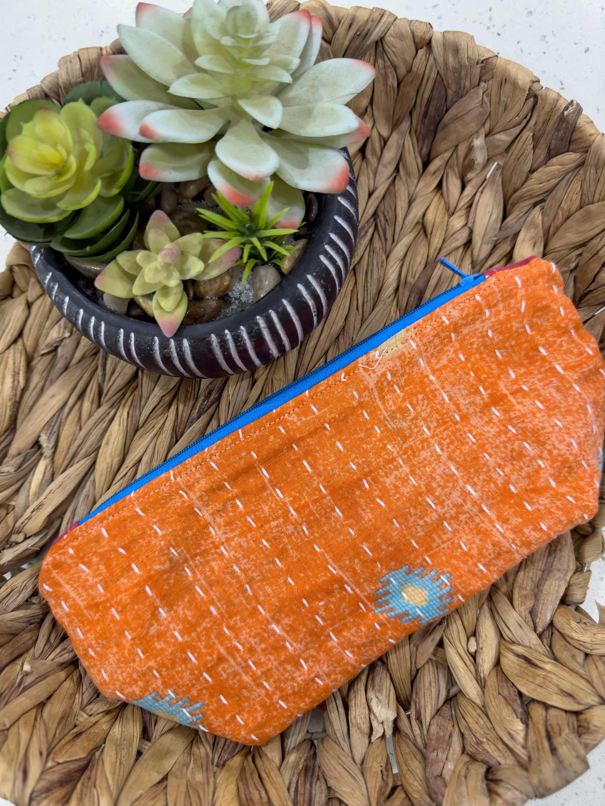 an orange purse sitting on top of a woven basket next to a succulent