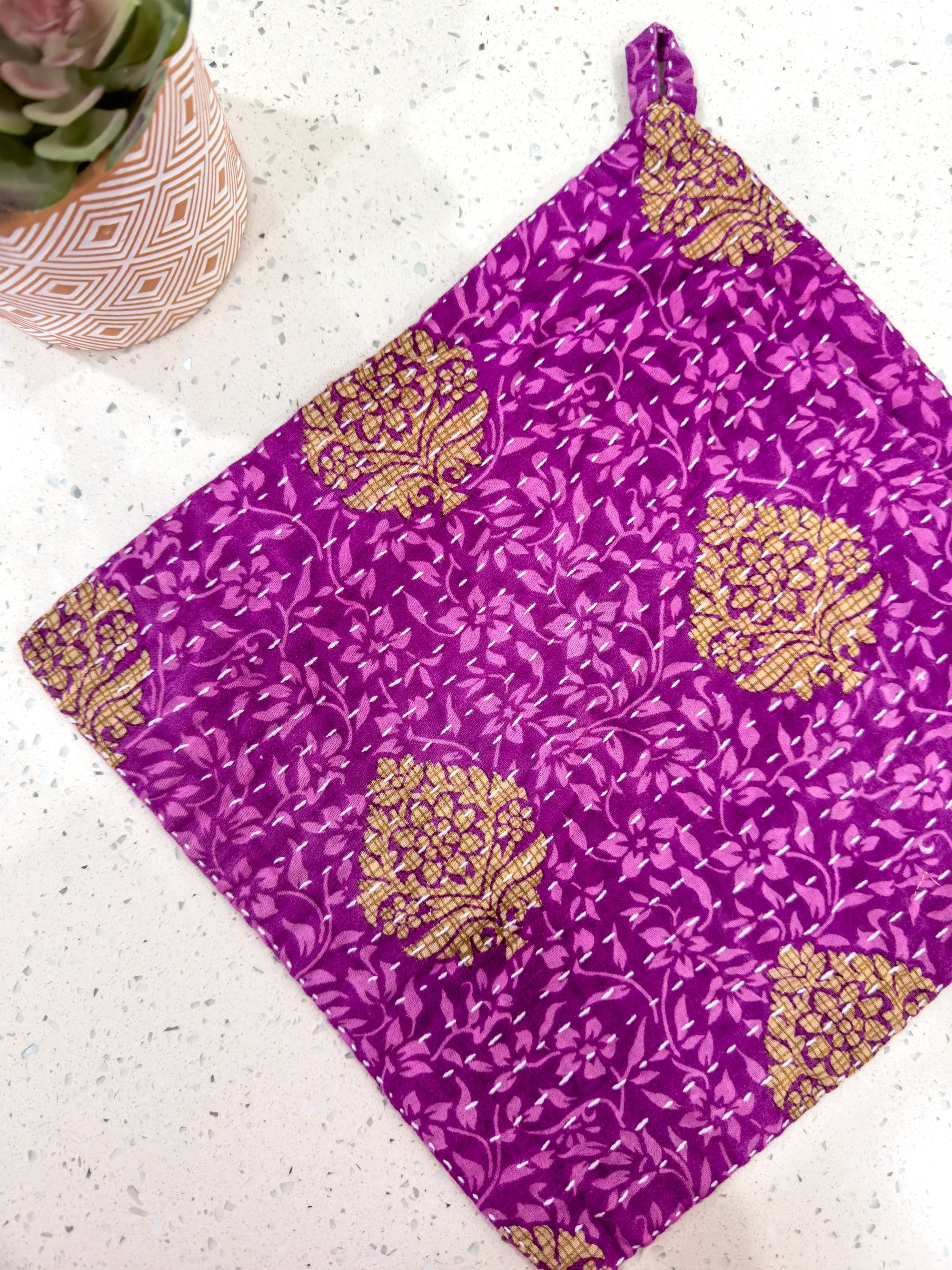 a purple cloth with gold designs on it next to a potted plant