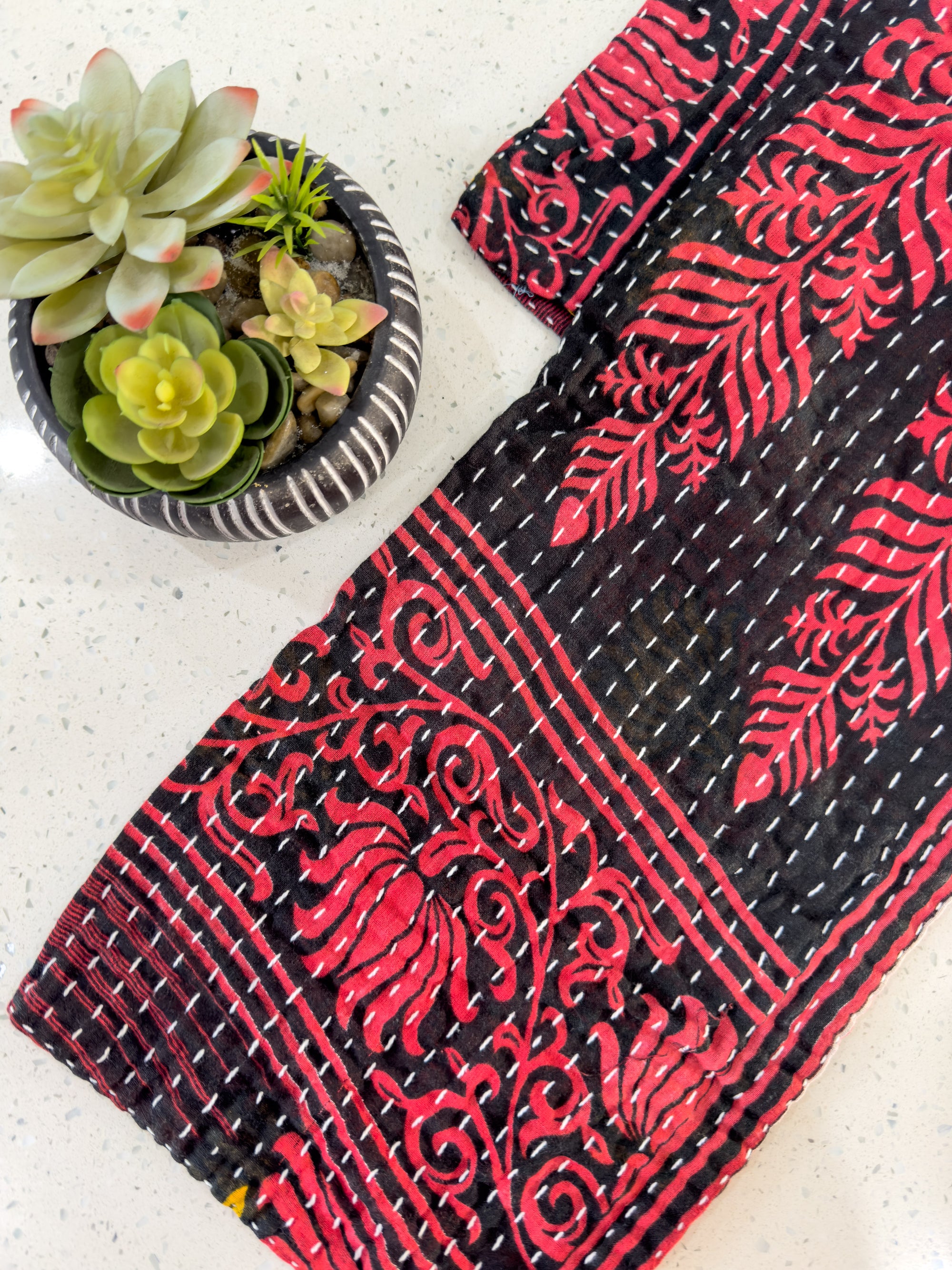 a red and black scarf next to a potted plant